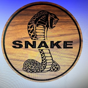 Puede incluir: Un letrero redondo de madera con un contorno negro y una imagen en blanco y negro de una cobra con la palabra "SNAKE" en letras negras.