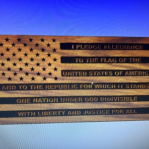 Puede incluir: Placa de madera con el diseño de la bandera estadounidense con estrellas y rayas. El texto "I PLEDGE ALLEGIANCE...WITH LIBERTY AND JUSTICE FOR ALL" está grabado en la superficie de madera. La placa es rectangular y tiene una veta de madera natural.