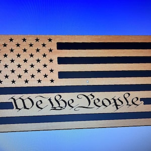May include: Wooden American flag with black stars and stripes. The words "We the People" are carved into the bottom of the flag.