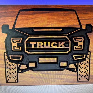 Puede incluir: Una parrilla delantera de camión negra y dorada con la palabra "TRUCK" en letras doradas.