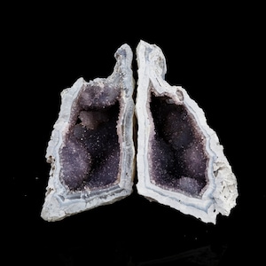 May include: A pair of amethyst geodes, each with a hollow interior lined with purple crystals. The geodes are split open, revealing the crystals inside.