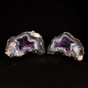 May include: Two amethyst geodes with purple crystals inside. The geodes are cut in half and show the interior crystals. The geodes are on a black background.
