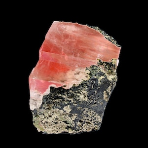 Könnte beinhalten: Ein rohes, natürliches Mineralexemplar mit einem leuchtend rosa, durchscheinenden Abschnitt auf einer dunklen, strukturierten Basis. Der rosa Abschnitt weist ein geschichtetes Aussehen mit Farbintensitätsvariationen auf. Die Basis ist eine Mischung aus Schwarz und Grün.