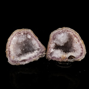May include: Two halves of a geode with a purple amethyst exterior and a white crystal interior. The geode is cut in half and the interior is visible.