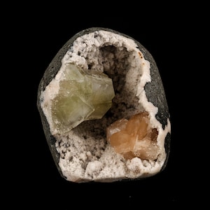 May include: A geode with a natural opening revealing a cluster of light green and orange crystals inside.