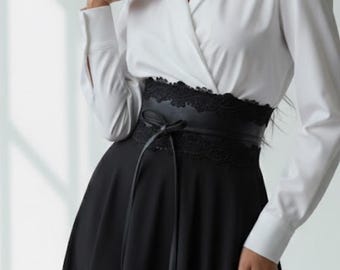 Könnte beinhalten: Ein langärmeliges Kleid mit einem weißen Oberteil mit Kragen in Wickeloptik und einem schwarzen Rock. Die Taille wird durch einen breiten schwarzen Gürtel mit Spitzenbesatz und einer mittigen Bindung betont, was einen Kontrast zwischen Ober- und Unterteil bildet.