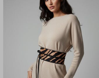Könnte beinhalten: Ein beiges, langärmeliges Strickkleid mit einem breiten Wickelgürtel im Obi-Stil. Der Gürtel ist schwarz mit einem beigen Tigerstreifenmuster und verfügt über lange, dünne schwarze Bänder, die vorne in der Mitte herabhängen.