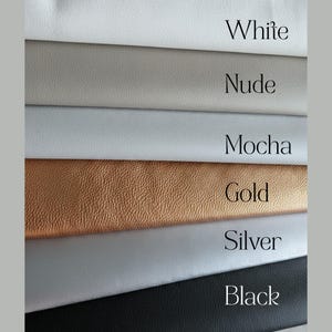 K&ouml;nnte beinhalten: Ein Stapel aus sechs lederartigen Materialmustern in verschiedenen Farben. Die Farben sind als White, Nude, Mocha, Gold, Silver und Black beschriftet. Jedes Muster zeigt eine eigene Textur, wobei das goldene Muster eine k&ouml;rnige Struktur aufweist.