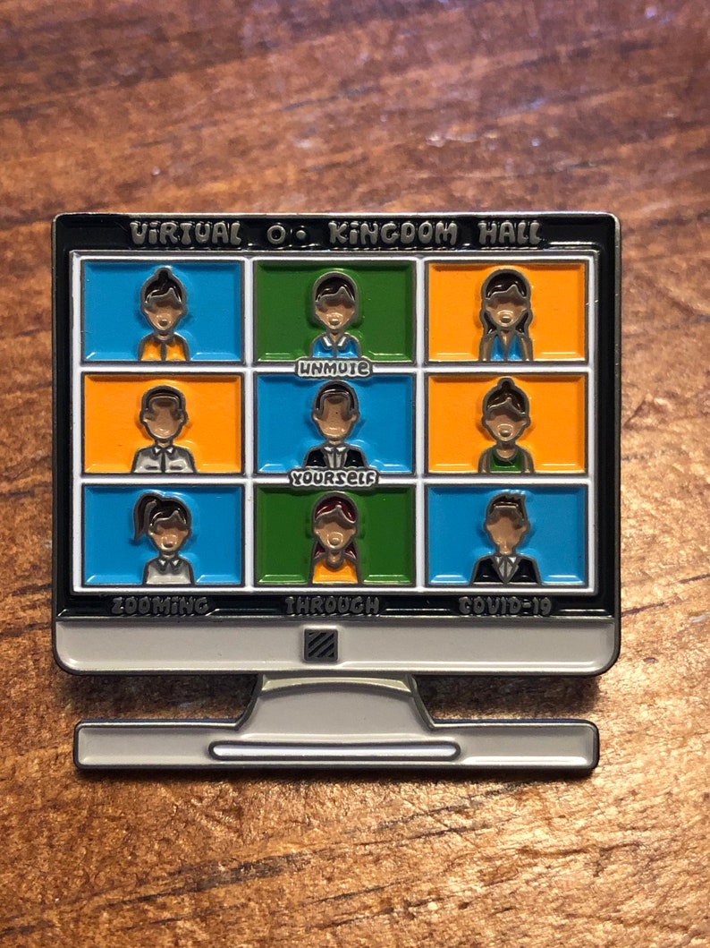Op de afbeelding: Een zilverkleurige computermonitor pin met een zwarte rand. Het scherm toont een videogesprek met negen deelnemers in kleurrijke vakken. Tekst bevat "Virtual O. Kingdom Hall", "Unmute Yourself", "Zooming Through Covid-19".