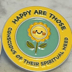 May include: A round, yellow enamel pin with the text "HAPPY ARE THOSE CONSCIOUS OF THEIR SPIRITUAL NEED." The pin features a smiling sunflower in the center, set against a teal background. The pin has a yellow border.