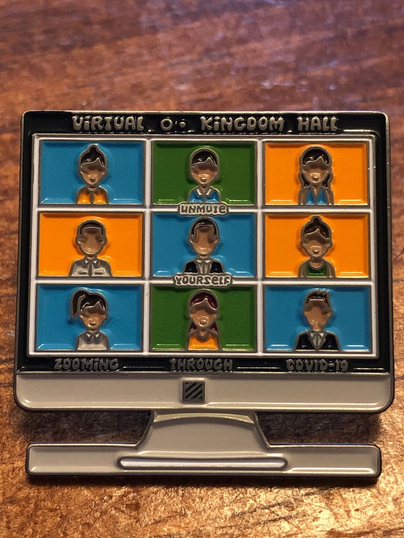 Op de afbeelding: Een speld in de vorm van een computermonitor met een zwarte rand. Het scherm toont negen kleine vakjes met cartoonfiguren. De tekst op de speld luidt "Virtual O Kingdom Hall", "Unmute Yourself" en "Zooming Through Covid-19".