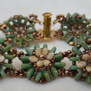 May include: A green and copper beaded bracelet with white flower accents. The bracelet is made with small, round beads and has a clasp closure.