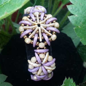 May include: A purple and cream beaded bracelet with a flower design. The bracelet is made with small, round beads and has a delicate, feminine look.