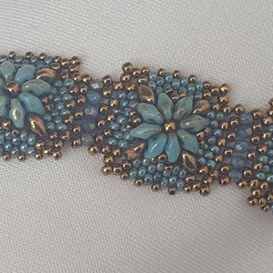 May include: A beaded bracelet with a repeating pattern of blue and gold flowers. The bracelet is made with small seed beads and features a delicate, intricate design.
