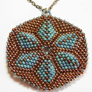 Può includere: Una collana con un ciondolo esagonale con un motivo geometrico di perline in rame e blu turchese.