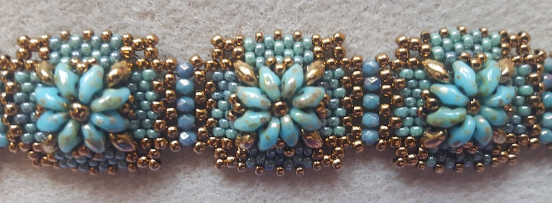 May include: A beaded bracelet with three blue and gold flower-shaped charms. The bracelet is made with small, round beads in shades of blue and gold.