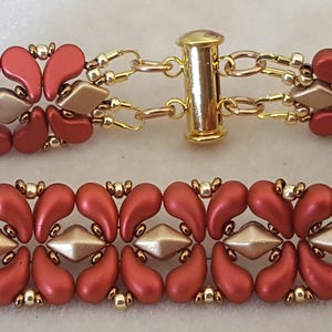 Op de afbeelding: Een rode en gouden kralen armband met een schuifsluiting. De armband is gemaakt met kleine, traanvormige kralen en heeft een herhalend patroon van rood en goud.