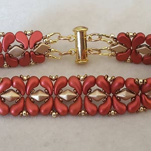 May include: A red and gold beaded bracelet with a toggle clasp. The bracelet is made with small, teardrop-shaped beads and features a repeating pattern.