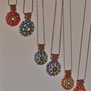 Può includere: Sei collane di perline con ciondoli di diversi colori. I ciondoli sono tutti rotondi e hanno un design floreale. Le collane sono appese su uno sfondo bianco.