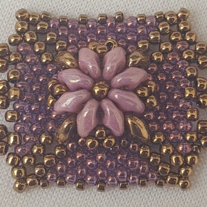 May include: A beaded bracelet with a repeating pattern of purple and gold beads, featuring a central flower design with a light purple color.