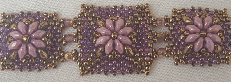 May include: A beaded bracelet with a repeating pattern of purple and gold beads, featuring a central flower design with a light purple color.