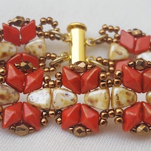 Op de afbeelding: Een kralenarmband met een gouden sluiting. De armband is gemaakt met rode, witte en gouden kralen in een geometrisch patroon.