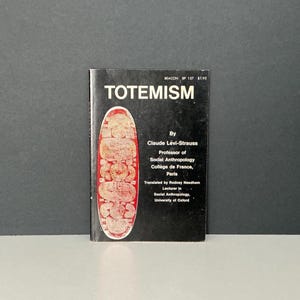 Può includere: Un libro vintage intitolato "TOTEMISM" di Claude Lévi-Strauss. La copertina è nera con testo bianco e una grafica rossa e beige. Il libro è un'edizione Beacon BP 157.