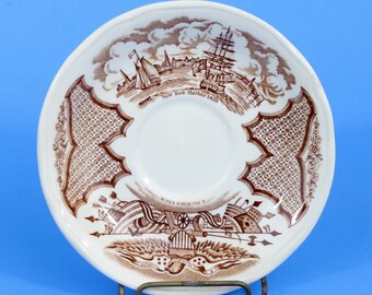 以下が含まれることがあります： 茶色の転写模様が施された白いソーサー。船のある港の風景と「New York Harbor 1830」の文字が描かれています。縁には装飾的な模様と愛国的なイメージがあります。