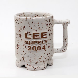 May include: White ceramic mug with brown speckled paint and the words "LEE SUPPLY 2004" in brown lettering.
