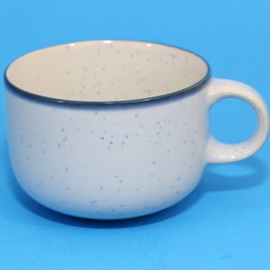 Könnte beinhalten: Eine weiße Keramiktasse mit blauem, gesprenkeltem Überzug und einem dunkelblauen Rand. Die Tasse hat eine abgerundete Form und einen Henkel.