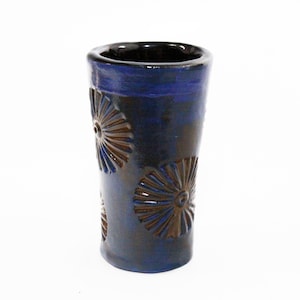 May include: A blue ceramic shot glass with a dark brown glaze and embossed flower designs.