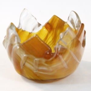 May include: A small, decorative glass bowl with a unique, petal-like design. The bowl features a blend of amber and clear glass, creating a layered effect. The rim has a jagged, uneven edge. The bowl is likely used for decorative purposes.