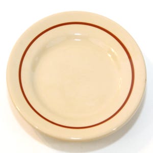 以下が含まれることがあります： クリーム色の丸いお皿で、細い濃い茶色の縁取りがあります。お皿はシンプルでクラシックなデザインで、食べ物を出すのに適しています。お皿はセラミックまたは磁器製です。