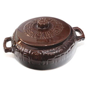 May include: A brown ceramic casserole dish with a lid. The dish has two handles and a decorative pattern around the base. The lid features a raised design and a small knob for easy handling. The dish is designed for cooking and serving.