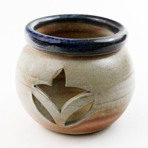 May include: A small, round, ceramic pot with a blue rim and a cut-out leaf design. The pot is glazed in a light gray color with brown accents.
