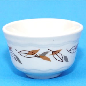 以下が含まれることがあります： 茶色、グレー、黒の葉模様が入った、波状の縁を持つ小さな白いセラミックボウル。 ボウルは丸みを帯びた底と滑らかで光沢のある仕上げです。 背景は無地の青色です。