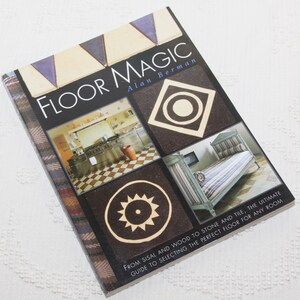 May include: A book titled "Floor Magic" by Alan Berman, with a colorful cover featuring various flooring options, including tile, wood, and sisal. The book's subtitle reads "From sisal and wood to stone and tile, the ultimate guide to selecting the perfect floor for any room."