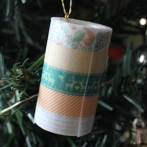 May include: A decorative Christmas ornament made from a roll of washi tape with a green, white, and orange pattern. The tape features a repeating design of reindeer and a heart.