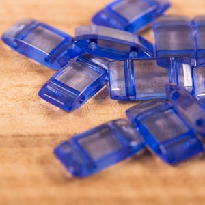 May include: A close-up of a pile of blue glass beads. The beads are rectangular and have a smooth, polished finish.