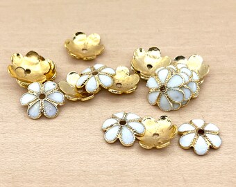 May include: A group of 12 gold flower-shaped bead caps with white enamel. The caps have a hole in the centre for stringing.