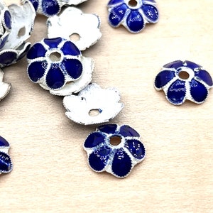 May include: A group of blue and silver flower-shaped metal bead caps. The caps have a small hole in the center and are designed to be used as decorative accents for jewelry making.