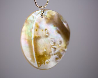 May include: A round, iridescent, mother-of-pearl pendant with a gold and white pattern. The pendant is attached to a silver loop.