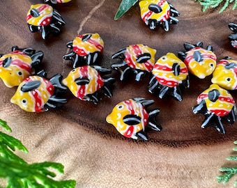 May include: A collection of ceramic fish charms with yellow, red, and black paint. The fish have a stylized design with black outlines and red and yellow stripes.