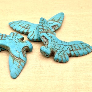 May include: A group of turquoise blue bird-shaped beads with a crackled finish. The beads are made of turquoise stone and have a rustic look.