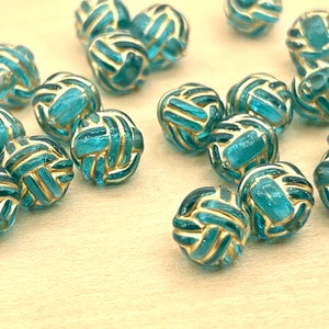 May include: A collection of teal blue glass beads with gold accents. The beads are shaped like a knot and have a textured surface.