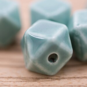May include: A group of five teal blue ceramic beads with a geometric shape. The beads have a hole in the center for stringing.