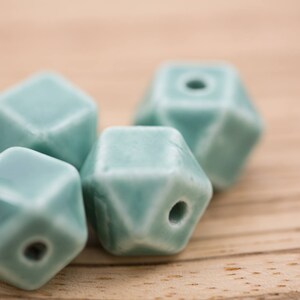 May include: A group of six teal blue ceramic beads with a geometric shape. The beads have a smooth, glazed finish and a hole in the center for stringing.