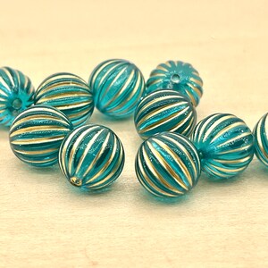 May include: A group of teal blue glass beads with gold stripes. The beads are round and have a shiny finish.