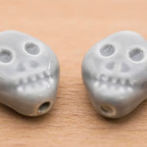 May include: Two grey ceramic skull beads with white eyes and teeth.