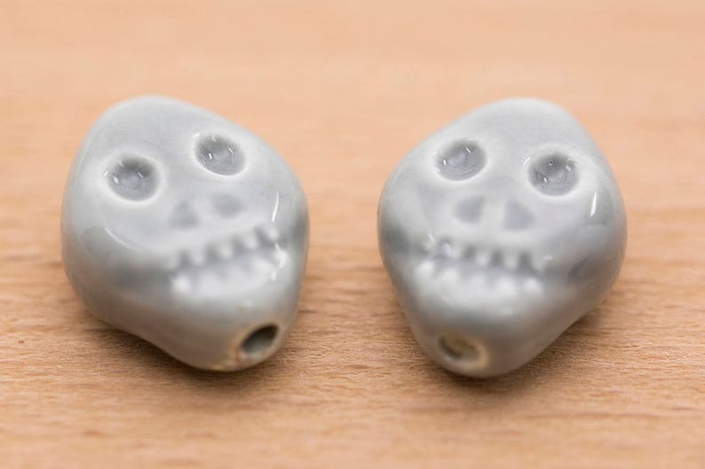 May include: Two grey ceramic skull beads with white eyes and teeth.